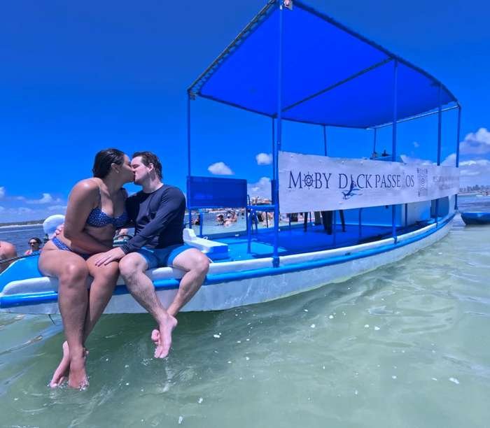 Casal na proa do barco durante passeio às Piscinas Naturais do Seixas
